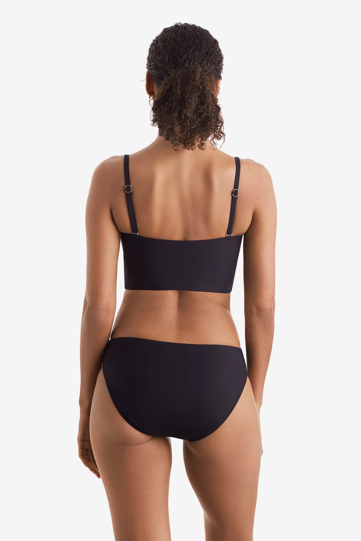 Woman faced away wearing a black midkini swim top with black swim bottoms