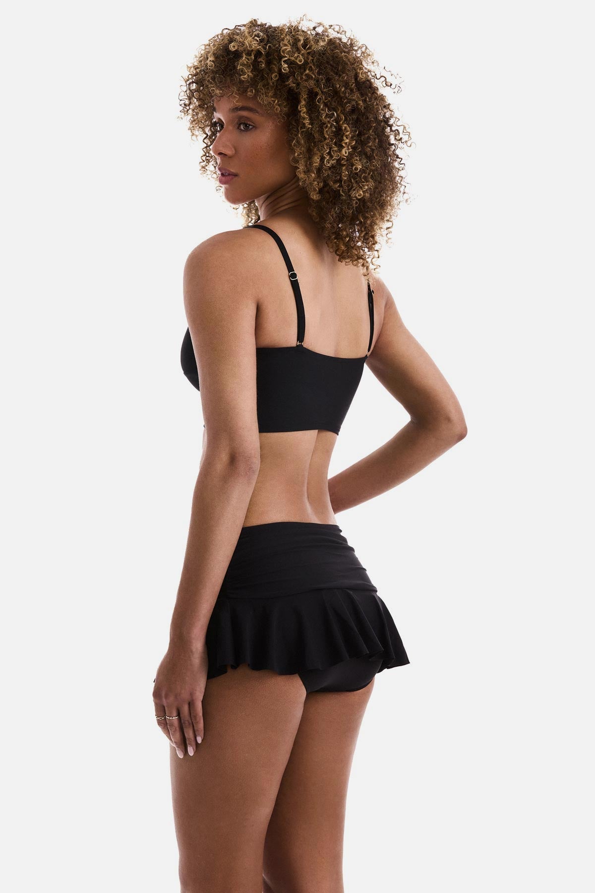 Woman turned left wearing a black midkini tankini swim top with matching skirted swim bottoms